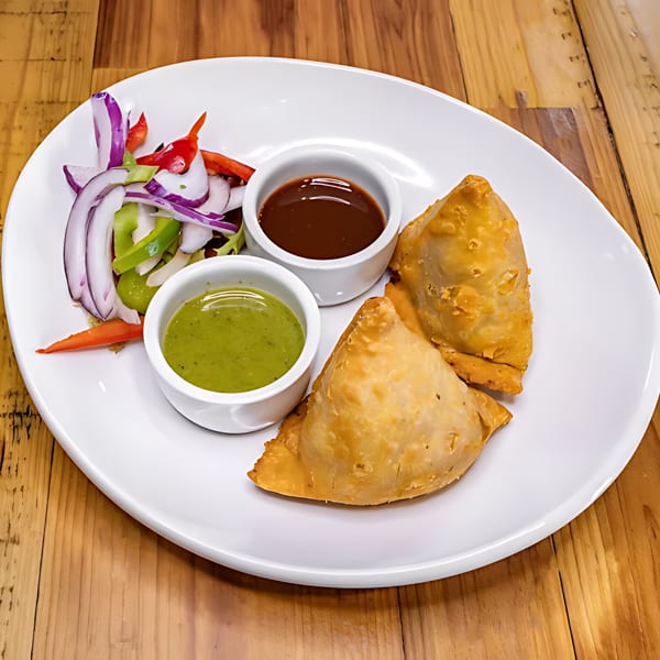 Two golden samosas with green and brown dipping sauces, and a side salad on a white plate.