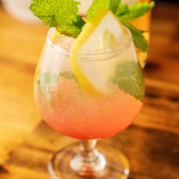A refreshing pink cocktail garnished with fresh mint and a lemon slice on a wooden table.