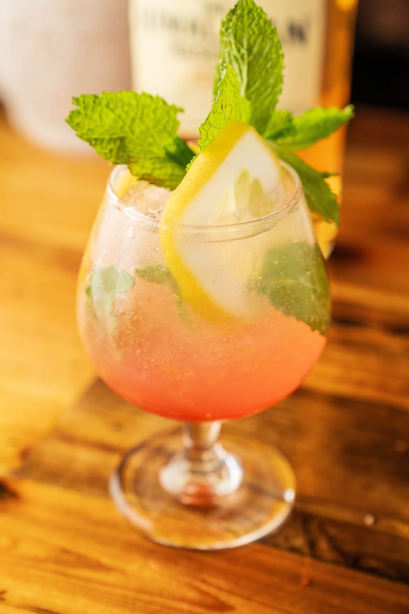 A refreshing pink cocktail garnished with fresh mint and a lemon slice on a wooden table.