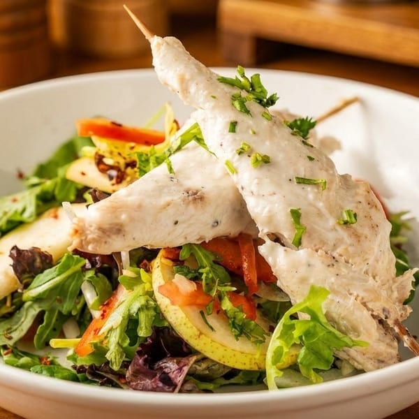 Chicken skewers with creamy sauce and chives, served over a fresh salad with pears and bell peppers.