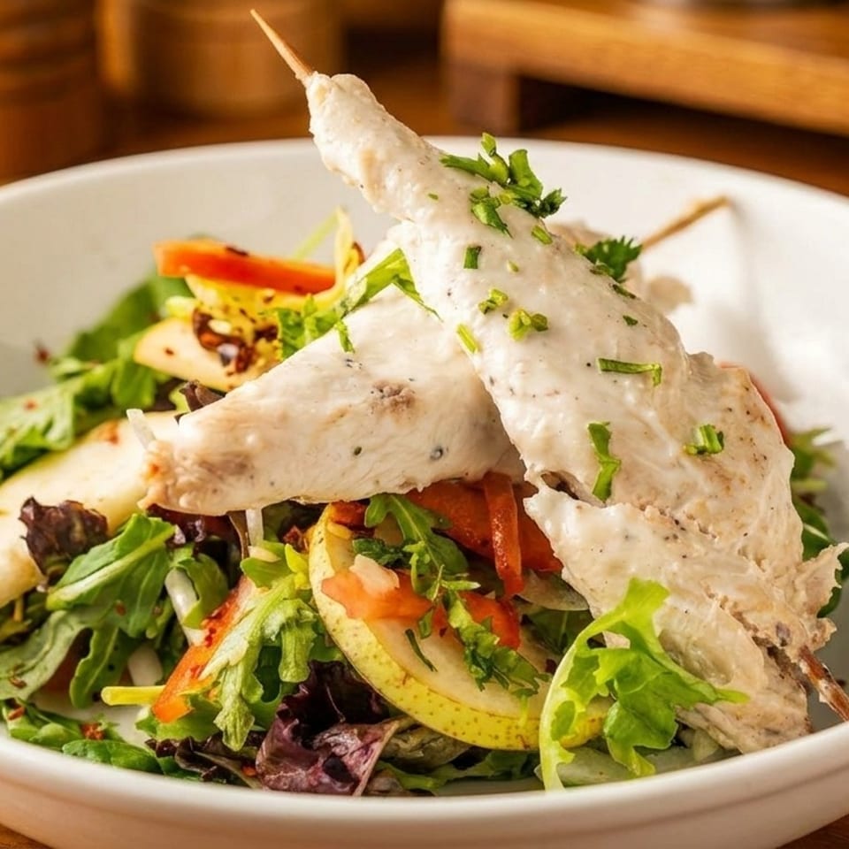 Chicken skewers with creamy sauce and chives, served over a fresh salad with pears and bell peppers.