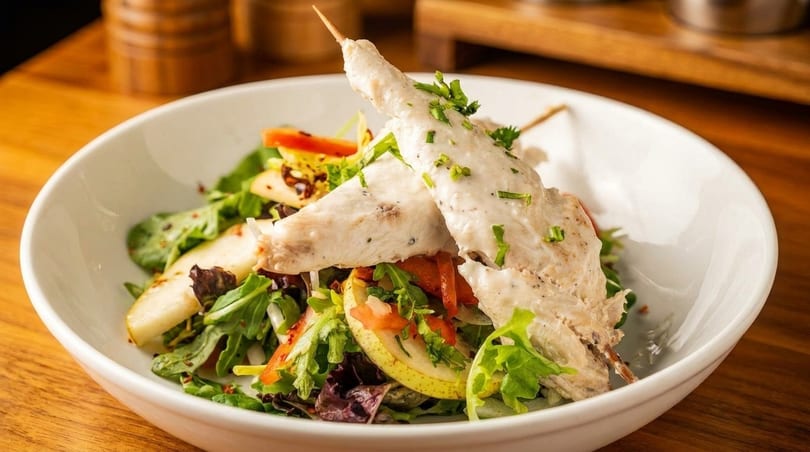 Chicken skewers with creamy sauce and chives, served over a fresh salad with pears and bell peppers.