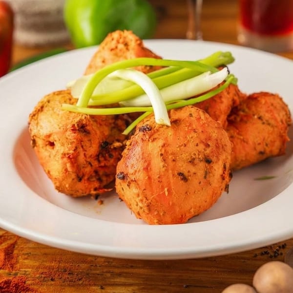 A white plate holds several orange-hued fried chicken pieces garnished with green onions on a wooden table.
