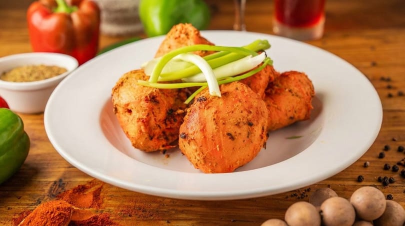 A white plate holds several orange-hued fried chicken pieces garnished with green onions on a wooden table.