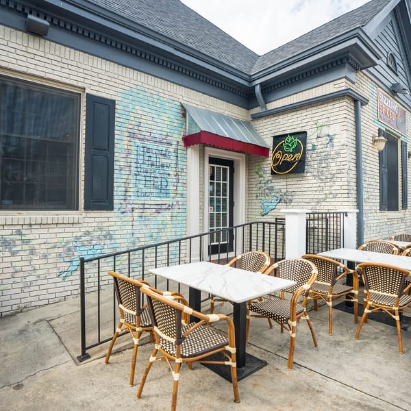 Outdoor patio of Sizzling Spices restaurant with tables, chairs, and a neon "Open" sign.