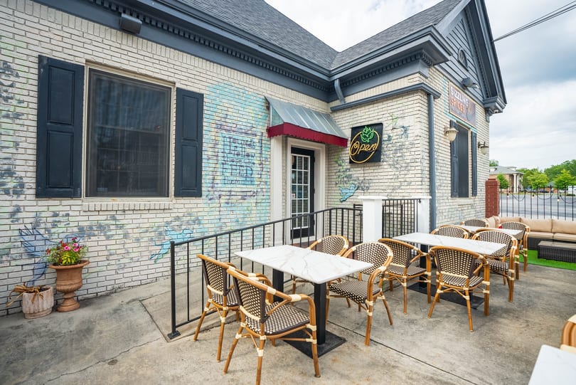 Outdoor patio of Sizzling Spices restaurant with tables, chairs, and a neon "Open" sign.