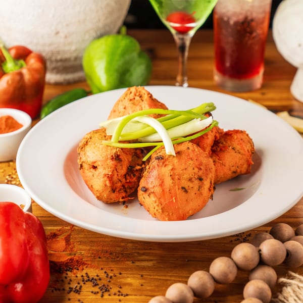 A plate of orange-colored fried food garnished with green onions, surrounded by spices and drinks.