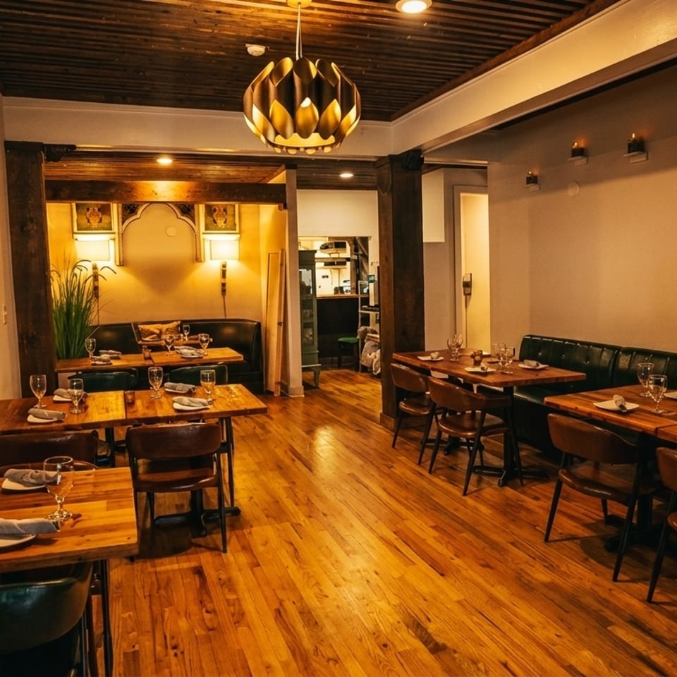 Warmly lit restaurant interior with wooden tables, dark leather banquettes, and a decorative ceiling light.