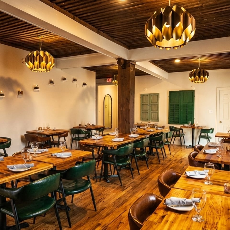 Warmly lit restaurant interior with wooden tables, green chairs, and decorative ceiling lights.
