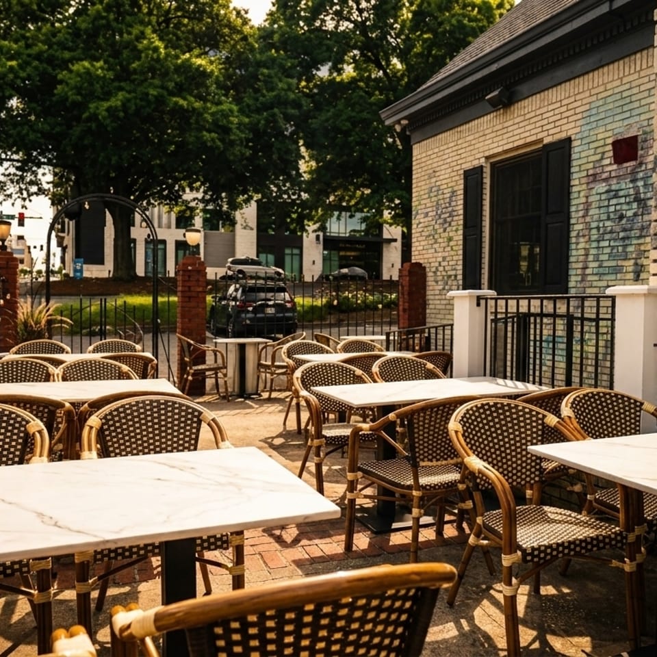 Outdoor patio dining area with marble-top tables and wicker chairs next to a brick building.