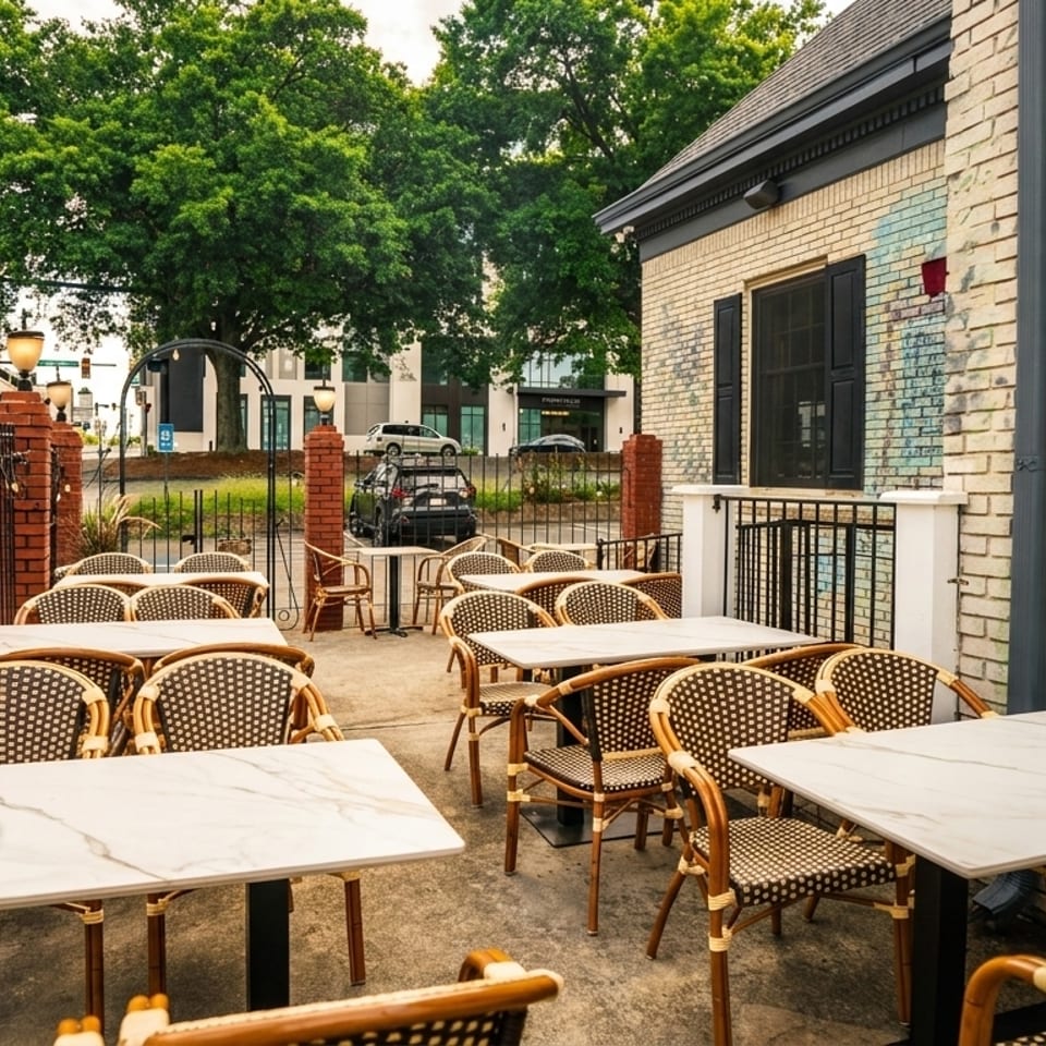 Outdoor patio dining area with marble-top tables and wicker chairs next to a brick building.